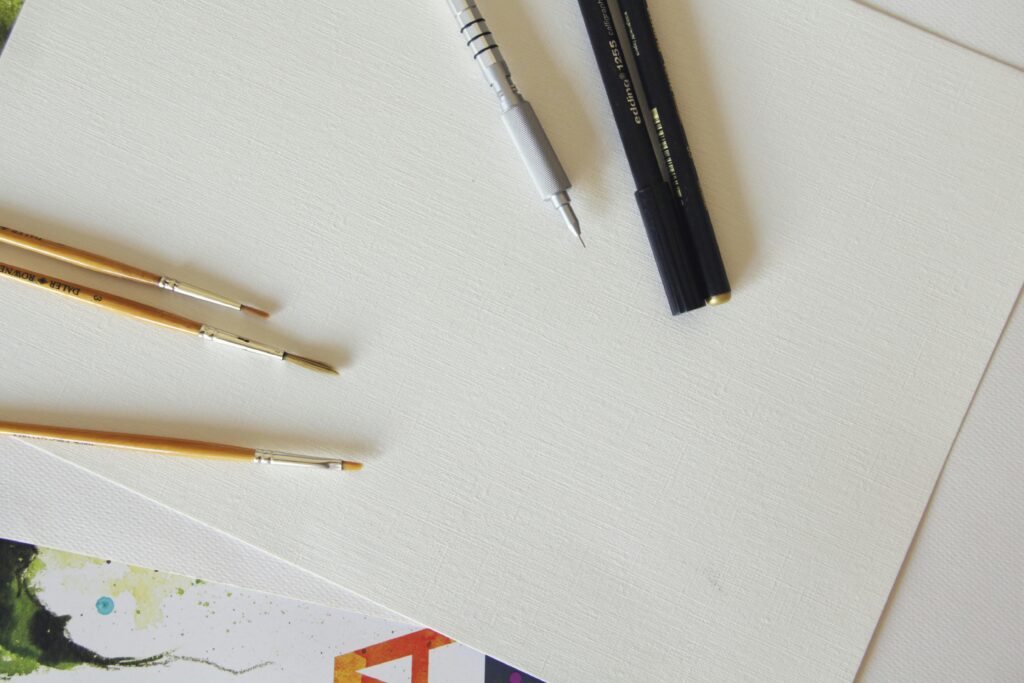 Creative workspace with blank canvas, pens, and paintbrushes for artists.