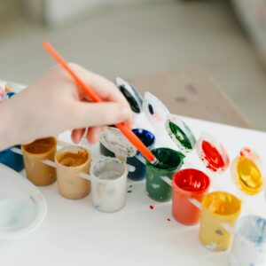 A child paints using a colorful watercolor palette, fostering creativity and fun.